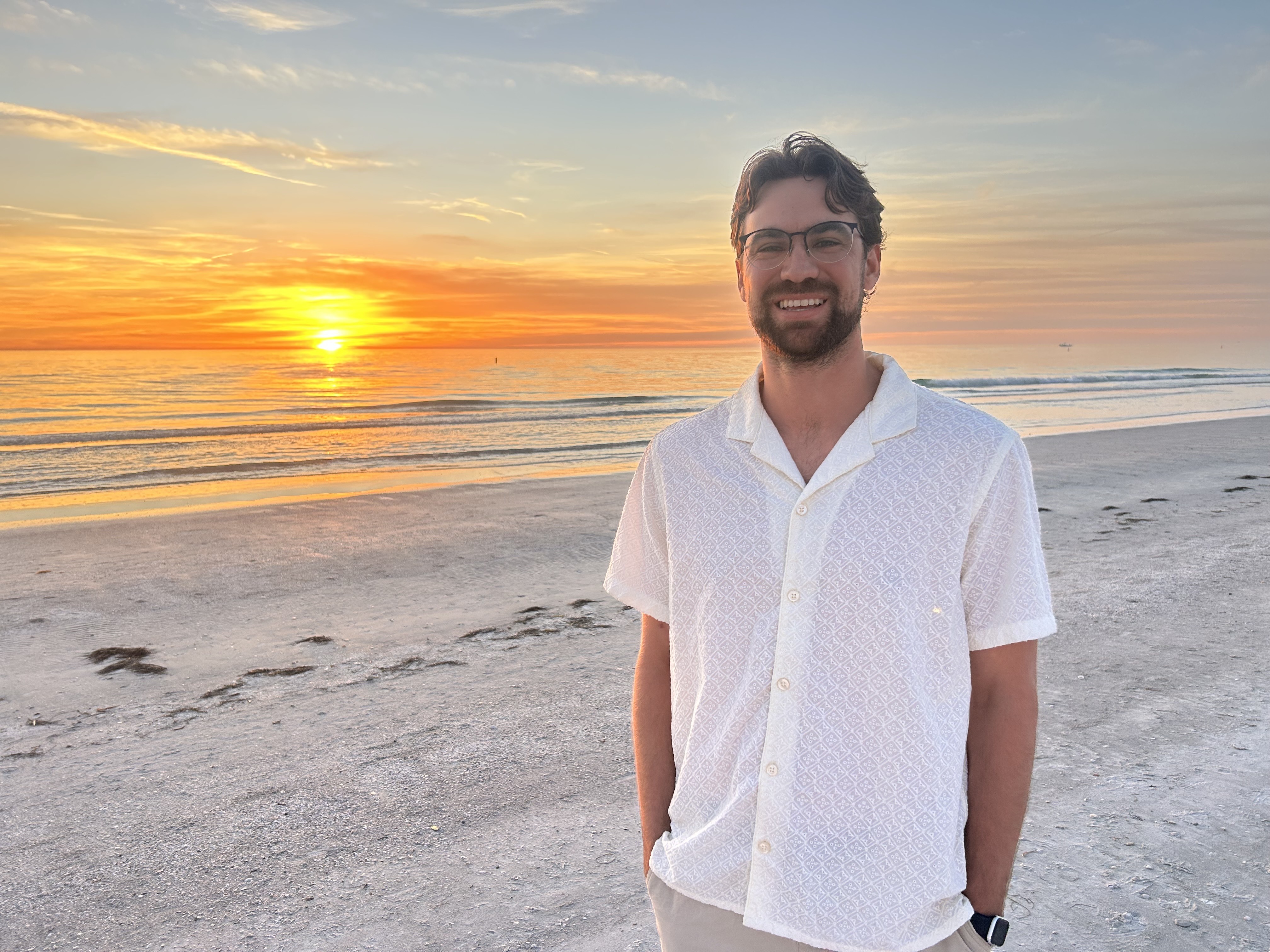 Luke Warner smiling on a beach at sunset.